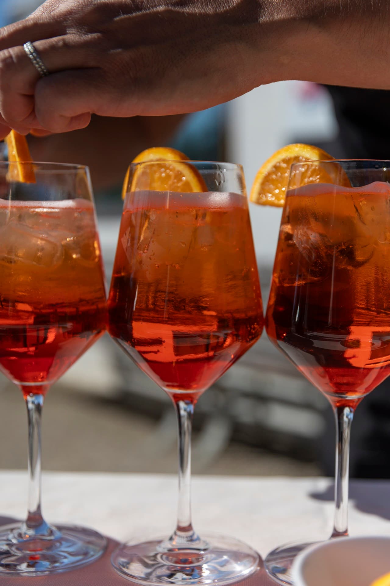 Tre calici di spritz guarniti con fetta d’arancia, pronti sul tavolo di partenza.
